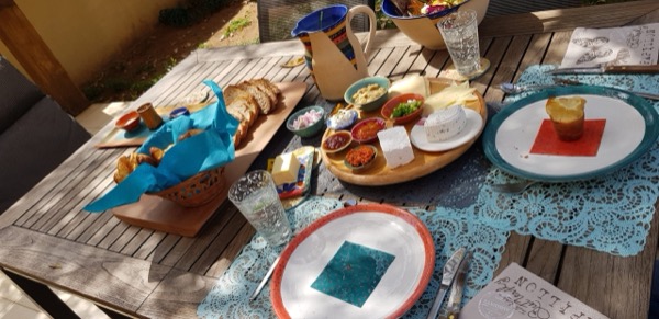 שולחן ארוחת בוקר כפרית ערוך בכלי קרמיקה, לחם, גבינות וממרחים בחצר