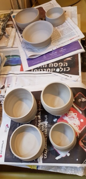 קערות וספלי חימר לא מזוגגים מתייבשים על עיתונים בתוך סטודיו הקרמיקה