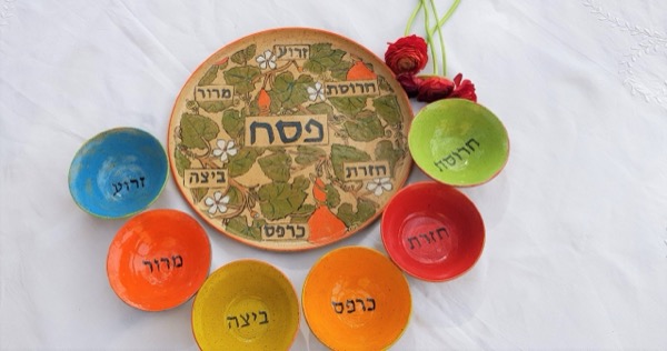 קערת סדר פסח מצוירת בעלים ורימונים לצד קעריות סימני החג